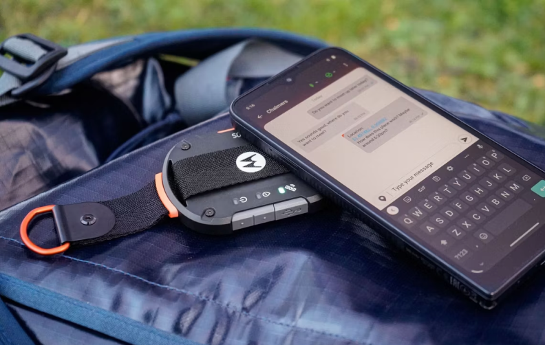 A smartphones sitting on top of the Motorola satellite dongle and a backpack.