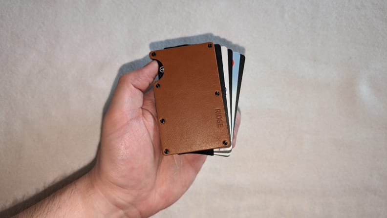 The Ridge Tobacco Leather wallet with cards sticking out of it being held in front of a white background.