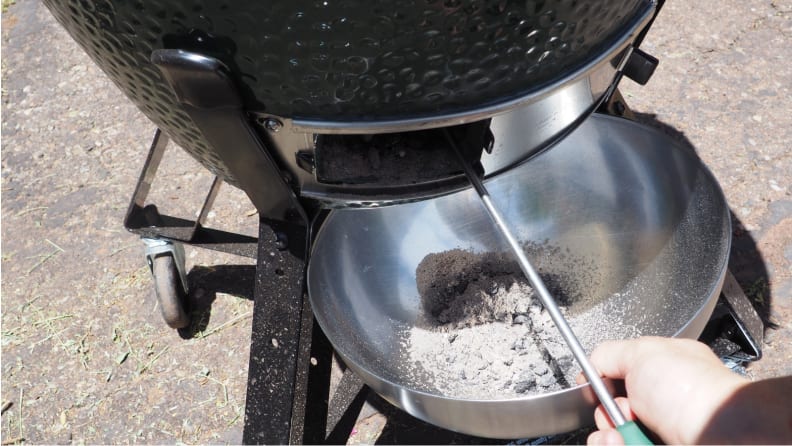 A person's hand using a wire brush to clean the ashes out of a kamado grill.