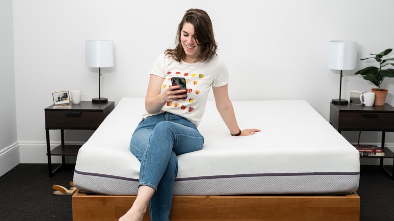 a person sits on the end of the Purple mattress on their phone