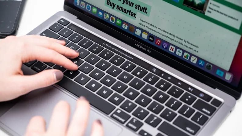 A pair of hands with painted fingernails type on a laptop keyboard