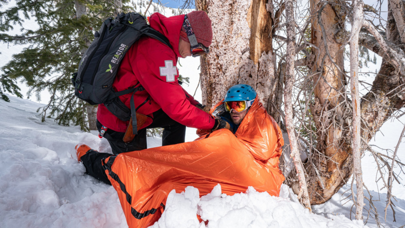 A paramedic helps a person into an emergency divvy on a snowy hill.