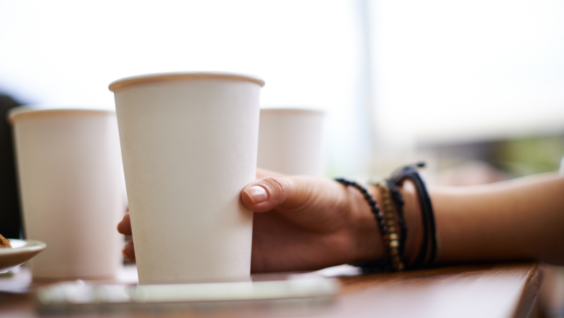 Person holding paper cup in hand on tabletop