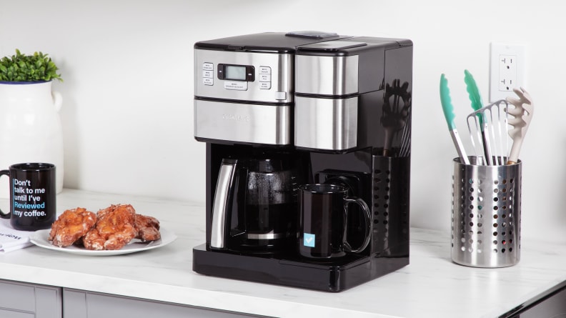 The silver and black Cuisinart coffee machine on a counter next to a coffee mug and plate of pastries.