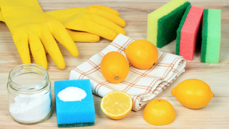 Yellow rubber gloves, salt, baking soda, sponges, and lemons on a kitchen counter.
