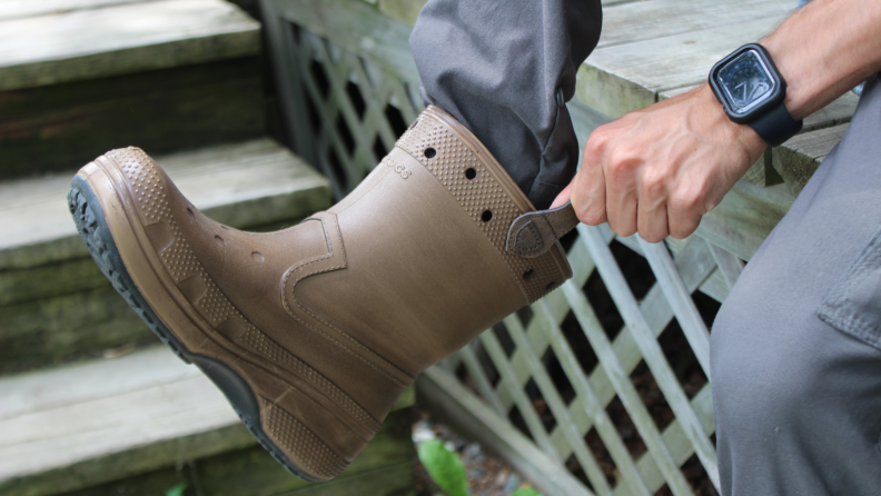 Hands pull a brown Huckberry x Crocs Classic Western Boot on to a foot.