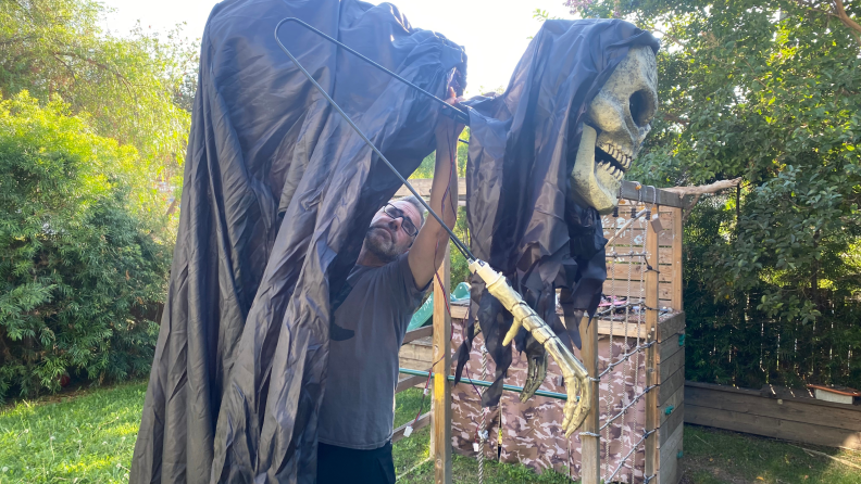A half-built 6-foot tall Grim Reaper stands hunched in a yard. A treehouse is in the background.