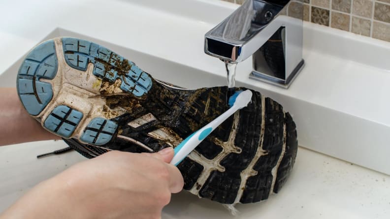 Cleaning dirty sneakers in a faucet with a toothbrush.