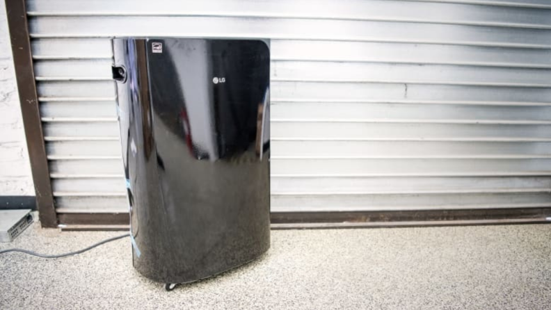 A black dehumidifier sitting on the ground with a filter behind it