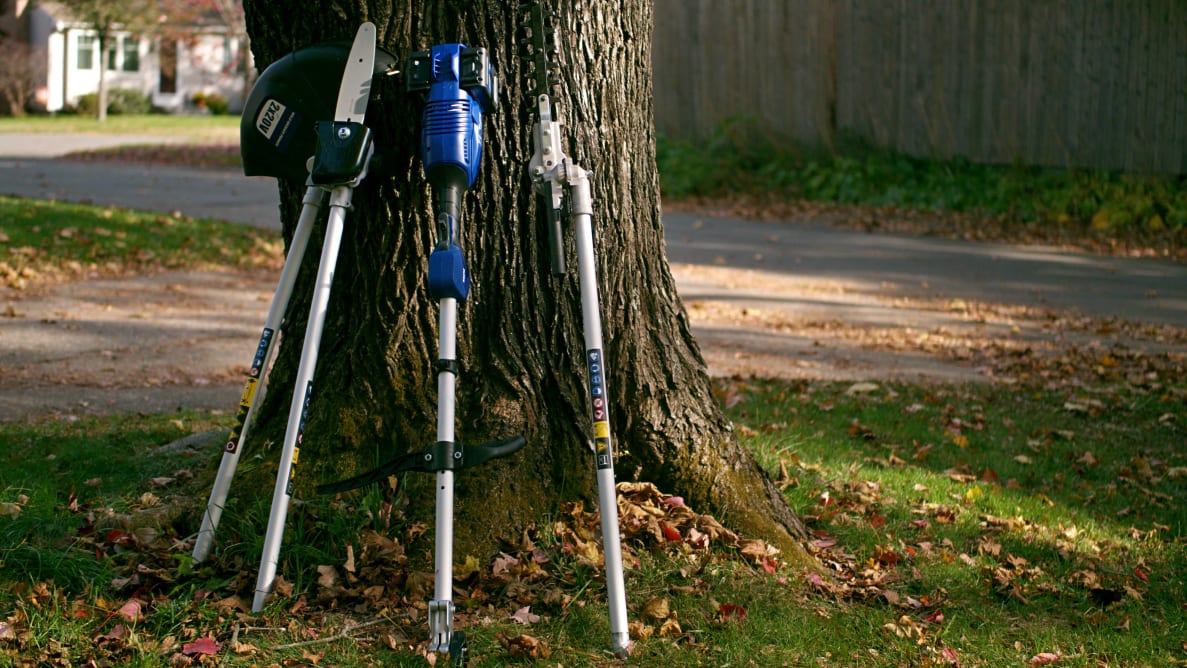 Four tool attachments stand against a tree in a suburban yard