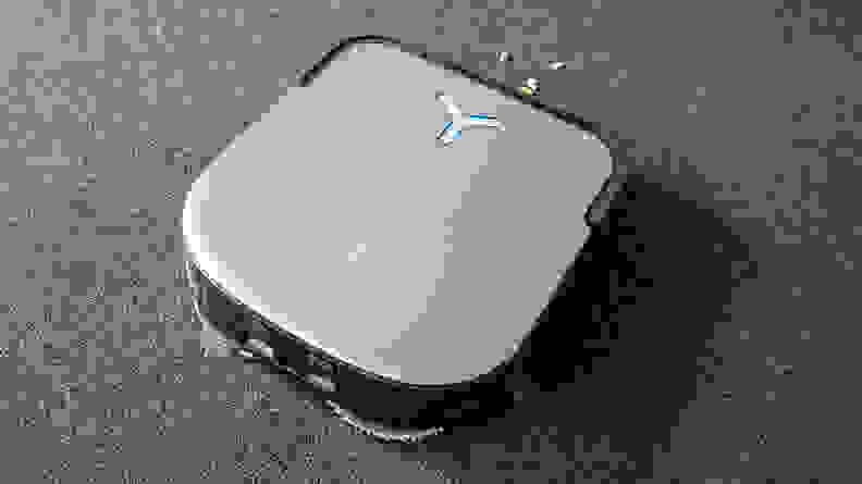A square, gray robot vacuum stands on  gray carpet