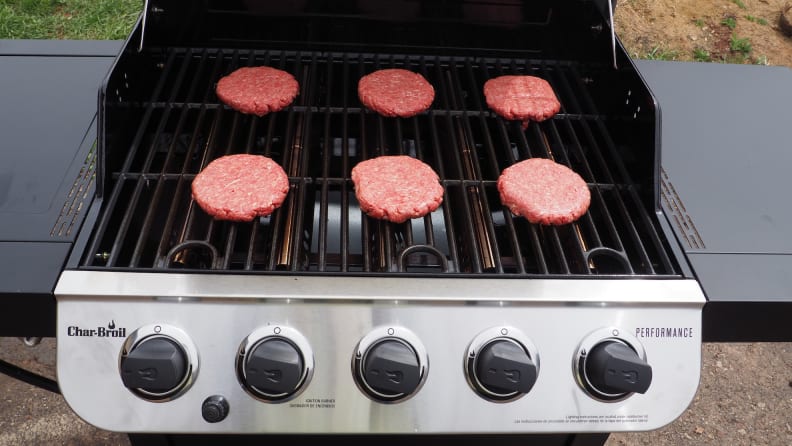Six raw burger patties laid out on an open gas grill