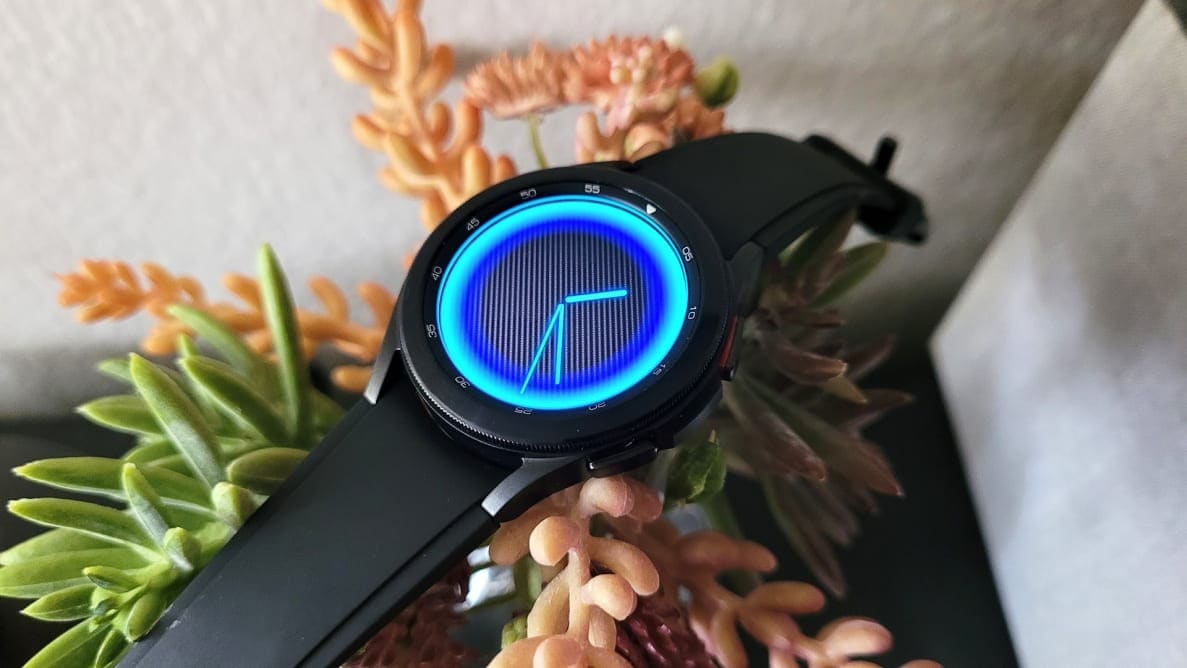 A black smartwatch with a circular, gleaming blue face sits on top of a floral background.