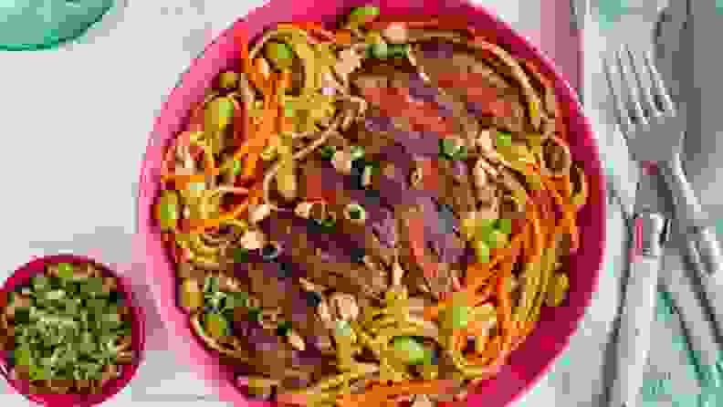 Sliced steak over udon noodles and carrots with edamame and scallions in a pink bowl.