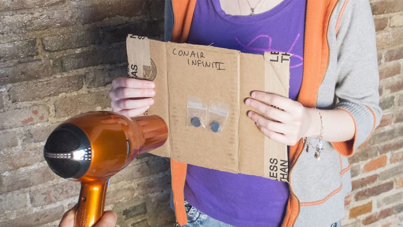 A person holding a piece of cardboard with heat sensors on it and a hair dryer pointing at the heat sensors.