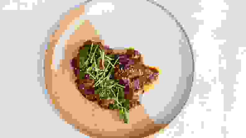 A top-down photo of a plate filled with braised oxtail topped with micro greens.