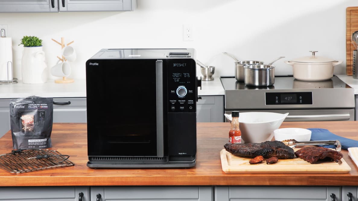 GE Profile Smart Indoor Smoker on a countertop surrounded by smoked meats and accessories