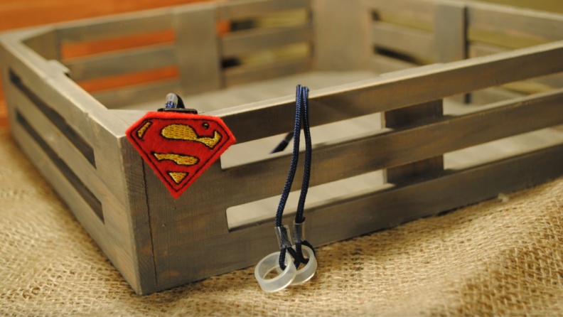 Superman themed hearing aid clips perched on wooden crate.