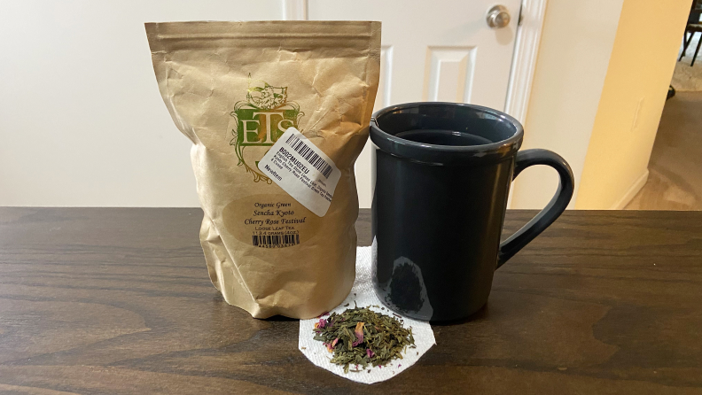 A big of English Tea Store Cherry Blossom Tea sits on a table next to a mug. Tea leaves sit under the mug on a paper towel.