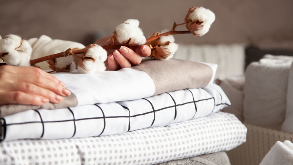 a person's hands atop a stack of sheets holding a sprig with cotton buds