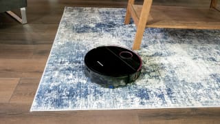 The Greenworks GRV-5011 Robot vacuum on a blue and white carpet, on a wooden floor.
