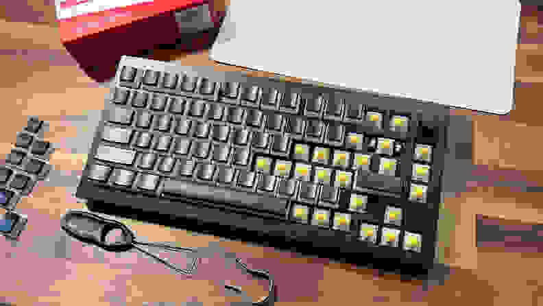 A keyboard half with keycaps and half with empty switches. There are also some keycaps sitting on the table where the keyboard is placed on.