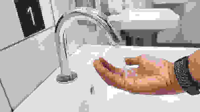 A persons hand under a running water coming out of a touchless sink faucet.