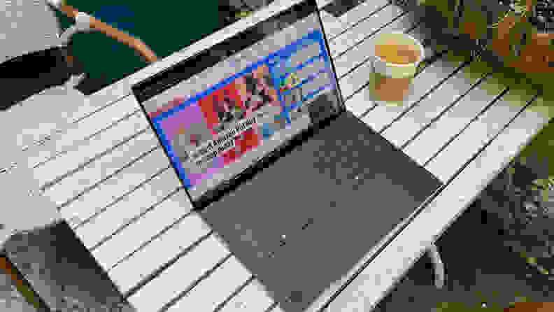 The Dell XPS 14 laptop opened to display a web browser on screen on a table outdoors next to a cup of iced coffee.