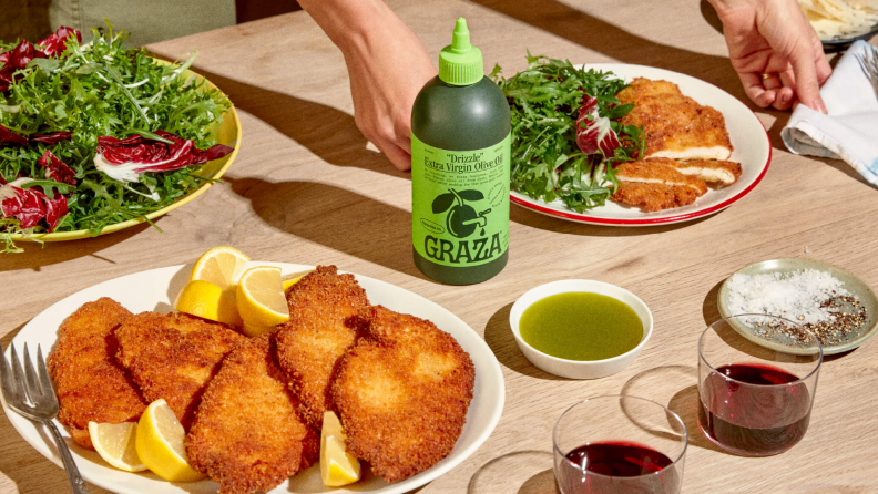 A bottle of Graza olive oil staged around a table full of food.