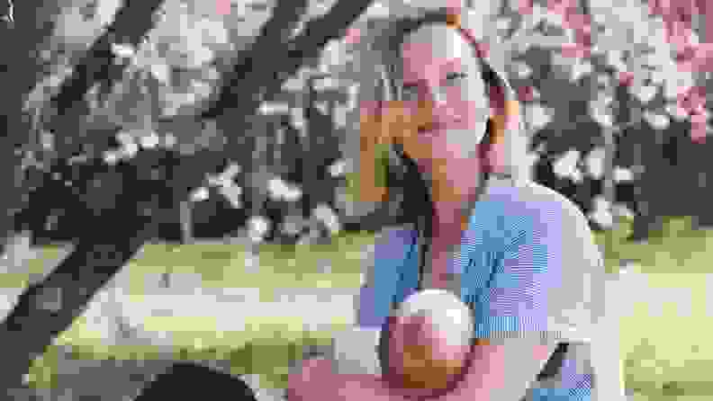 A woman breastfeeding her baby in a park.