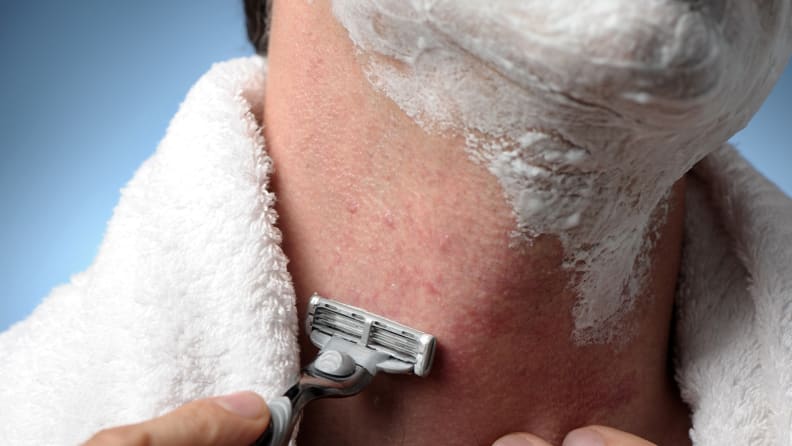A person shaving their beard with a razor and shaving cream.