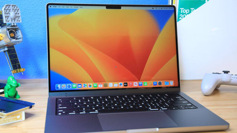 The Apple MacBook Pro 14 (2023) open, sitting on a wood table, with a picture of orange and blue shapes on the screen.