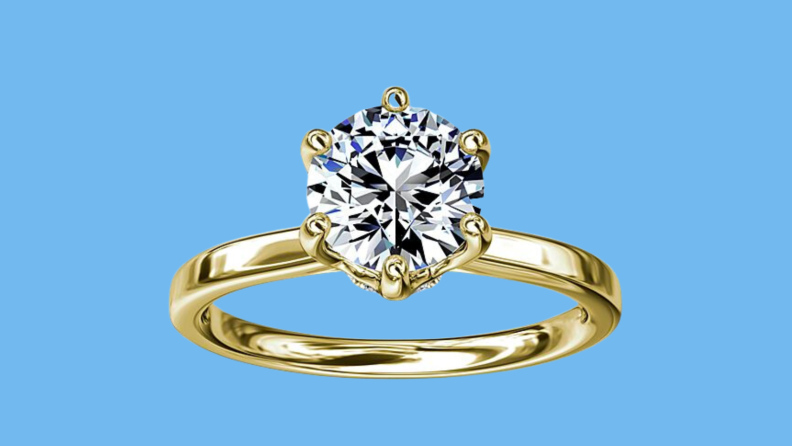 An image of a gold wedding band with a round diamond set into a six-pronged setting, with a barely-there line of diamonds peeping out from beneath the central stone.
