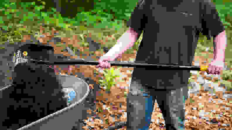 A person scooping dirt into a wheelbarrow using a shovel