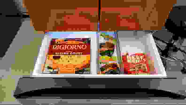 The bottom drawer (freezer) of the fridge opened showing off some Digiorno pizza and beef.