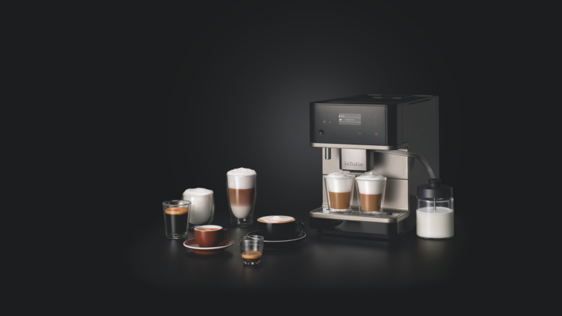 There are various coffee drinks, from the left: Americano, espresso shots, mocha, and latte. In the center, a Miele CM6 Milk Perfection is making two coffee drinks by frothing a glass of milk next to it.