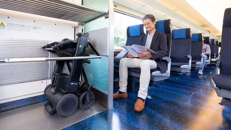 A person rides a train with their wheelchair folded on the side.