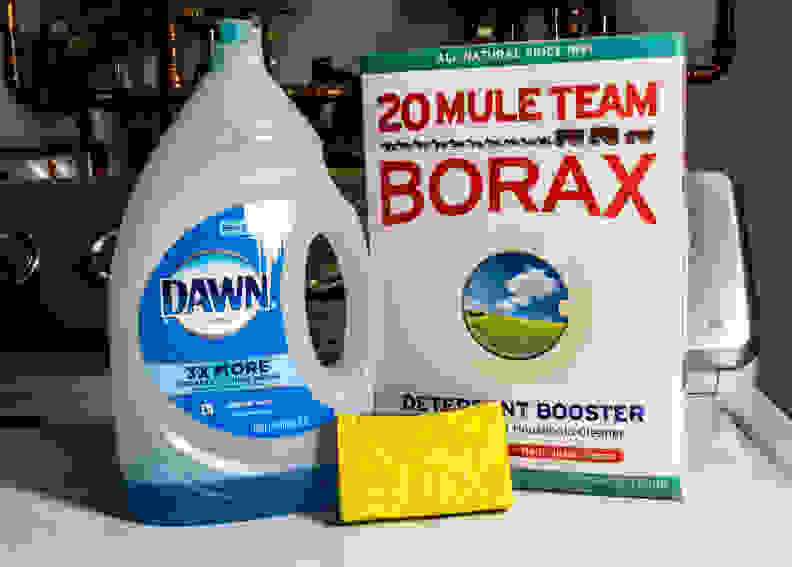 A bottle of Dawn dish soap, a box of Borax, and a yellow sponge sit on top of a washing machine.