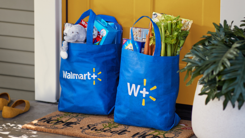 Two blue Walmart shopping bags filled with groceries sit in front of a door.