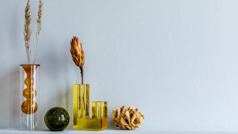 Yellow-hued items like vases and flowers sit on a shelf against a grey wall.