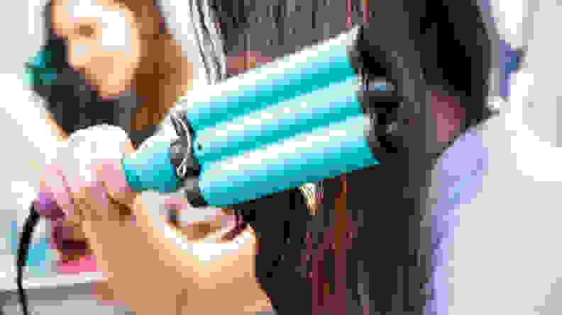 A closeup on the turquoise barrels of a hair waver in long brown hair.