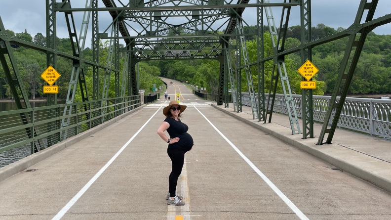 A smiling pregnant woman standing in the middle of bridge.