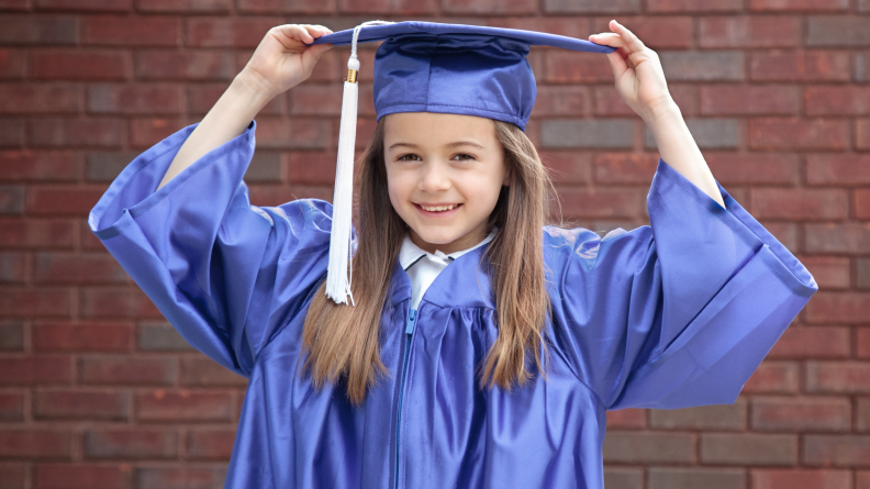 A child proudly puts on her graduation cap