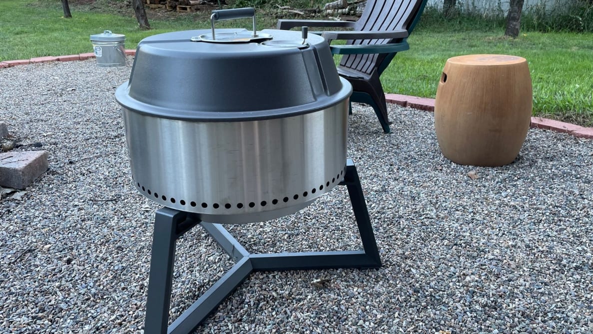 A portable charcoal grill sits on a pebble-covered yard.