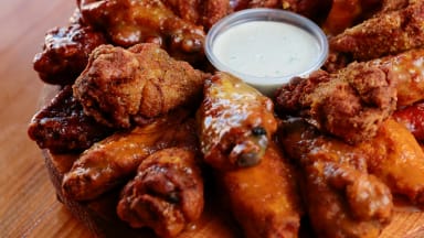 Wood plate of chicken wings running in stacked rings around a small plastic container of ranch dressing