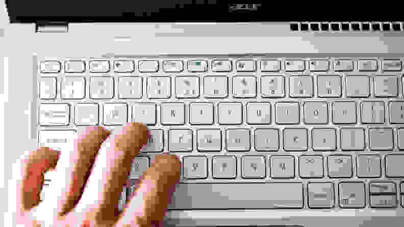 A close up of a person's left fingers touching a silver laptop's keyboard.