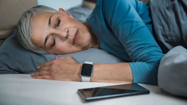 a person sleeps wearing a fitness tracker next to their phone