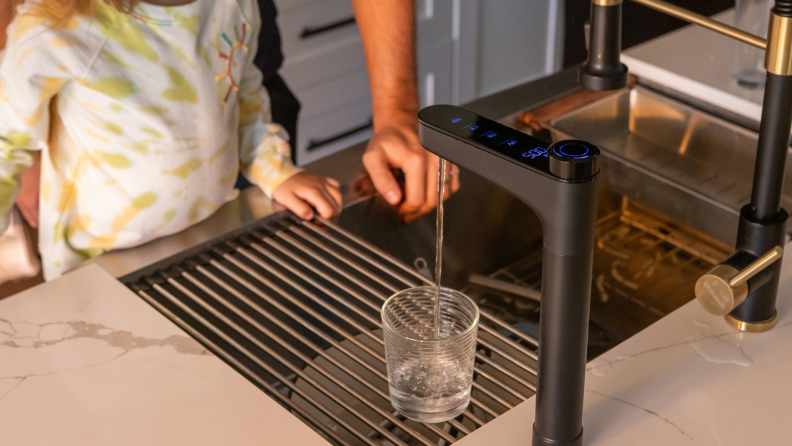 A child and adult fill a water glass from the faucet over a kitchen sink using the Waterdrop X series filter