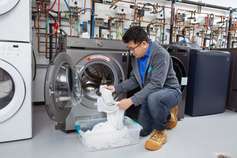 A person loading a front load washer with laundry.