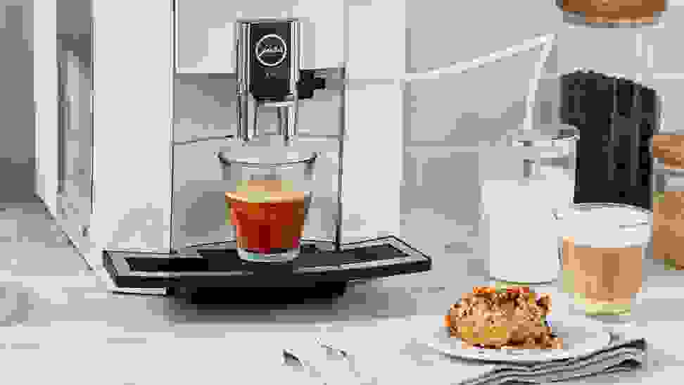 Close-up photo of a Jura high-end coffee maker in action. A scone sits on a small plate beside it.